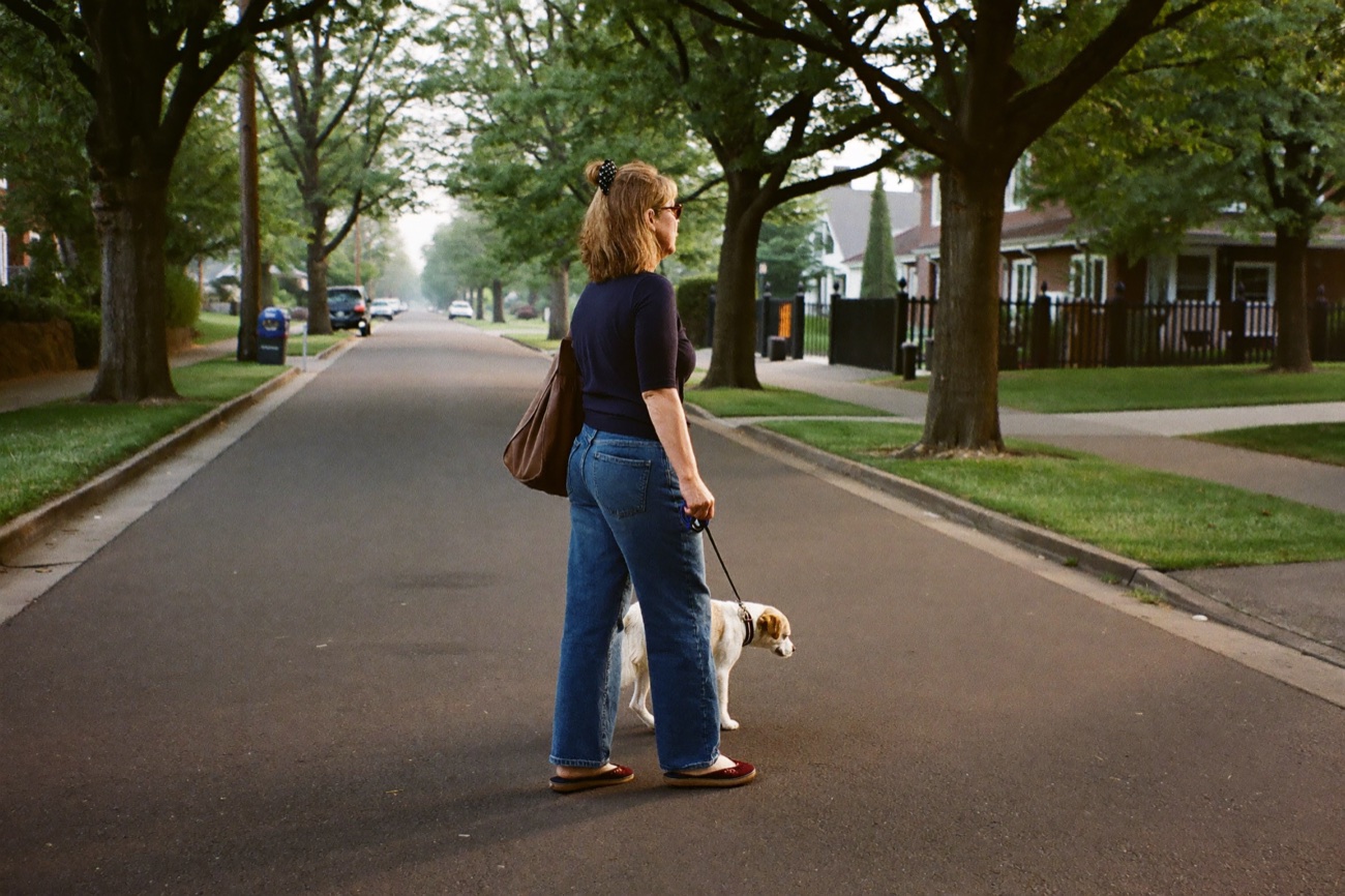 A relaxed woman about sixty walking her dog on a quiet tree-lined street in the morning.