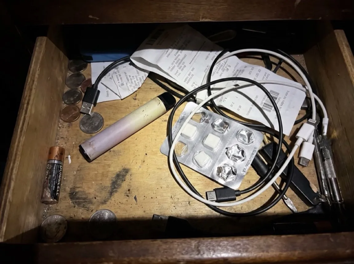 A used disposable vape pen and a half-punched nicotine gum blister pack tossed into a cluttered junk drawer under a harsh phone flash.