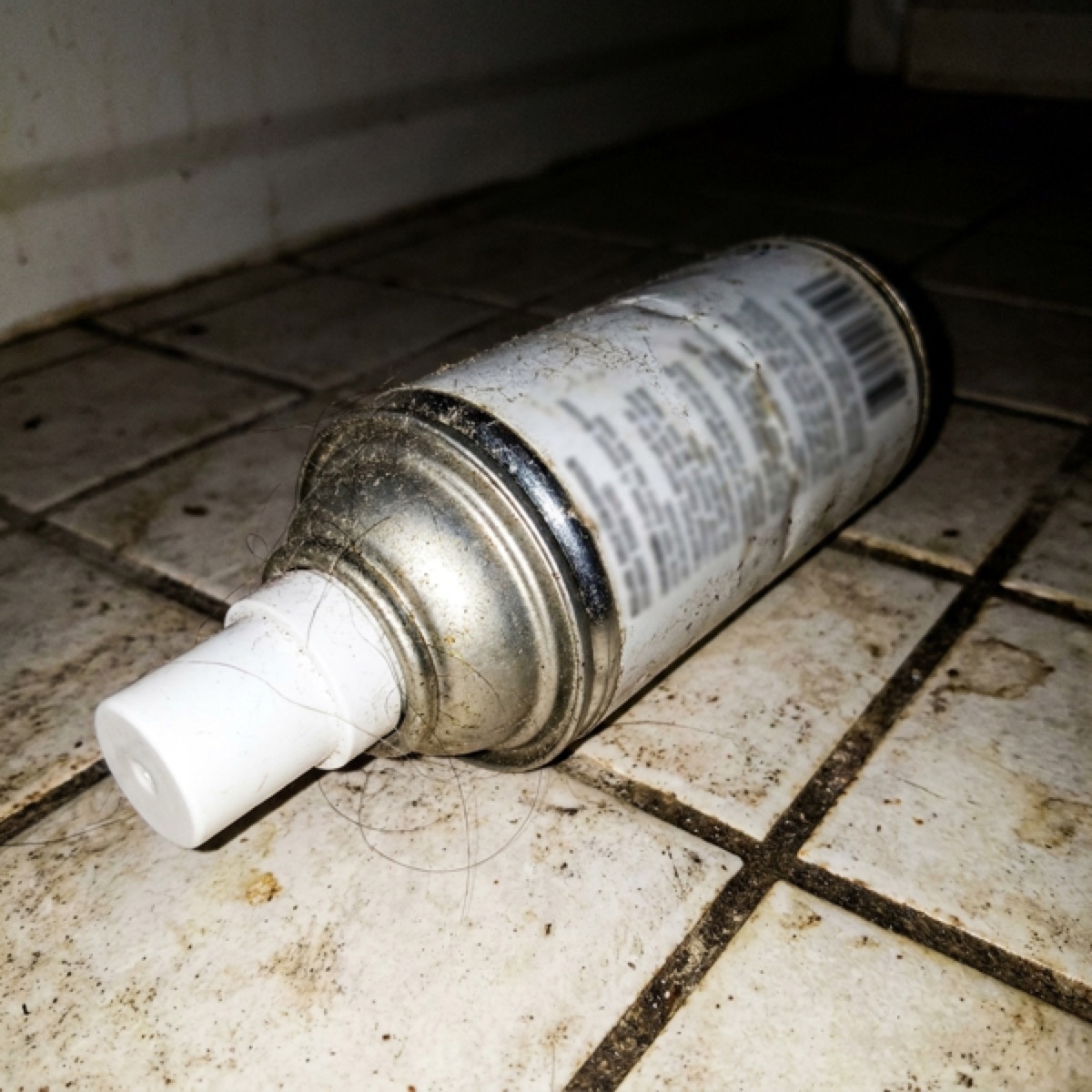 A dented dusty can of oxygen lying on a dirty bathroom floor.