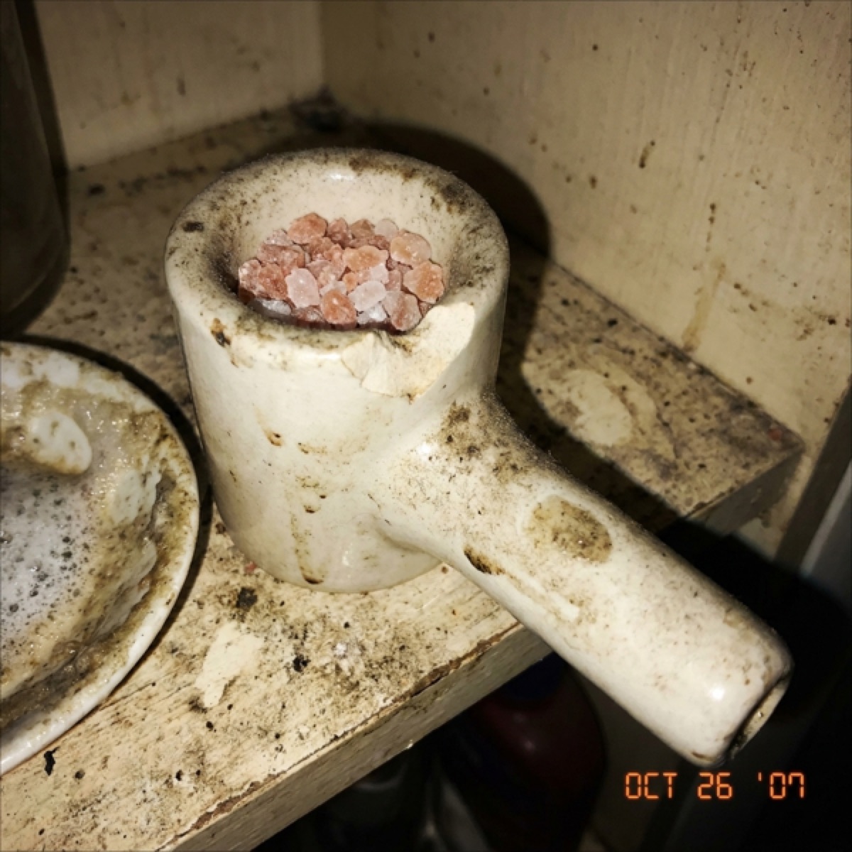 A dusty chipped ceramic salt inhaler with fingerprints on a grimy shelf.